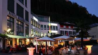 Abendliche Stimmung vor der Brasserie Burg in Vaduz mit beleuchteter Terrasse und Gästen unter Sonnenschirmen.