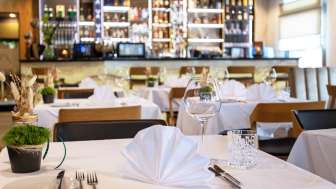 Geschmackvoll gedeckter Tisch im Restaurant Alpspitz mit Blick auf die Bar im Hintergrund.