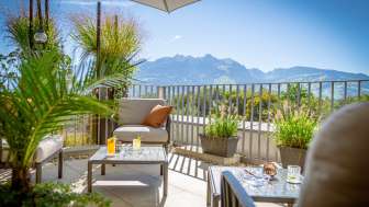 Sonnige Terrasse mit modernen Loungemöbeln und Alpenpanorama im Hintergrund