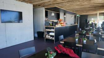 Moderner Gastraum mit dunklen Tischen, frischen Blumenarrangements und rustikalem Holzdach