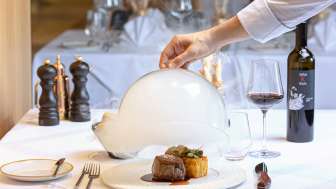 Serviertes Gourmetgericht mit Fleisch und Beilage, dekorativ unter einer weißen Cloche im edlen Restaurant Alpspitz angerichtet.