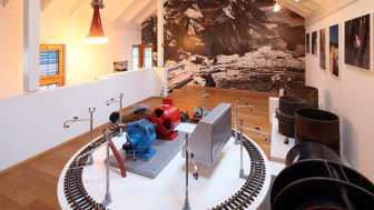 Modell einer Turbine auf einer Ausstellungsplattform im Lawena Museum, im Hintergrund historische Schwarzweißaufnahmen.