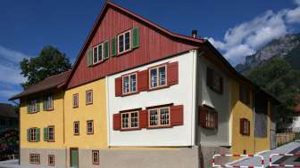 Traditionelles Landweibels-Huus in gelb-roter Fassadengestaltung vor Bergkulisse in Liechtenstein.