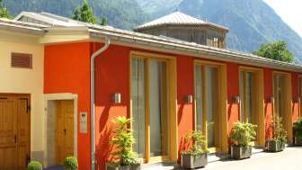 Außenansicht des Gasometer Kulturzentrums mit farbenfroher Fassade und Alpenpanorama im Hintergrund.