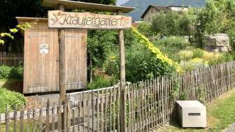Holzschild mit Aufschrift „Kräutergarten“ am Eingang des liebevoll angelegten Gartens in Mauren, umgeben von Natur und Bergen.