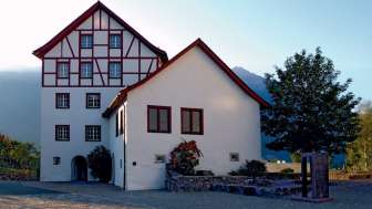 Historisches Gebäudeensemble der Pfrundbauten mit Fachwerkfassade und Bergkulisse in Liechtenstein bei Abendlicht.