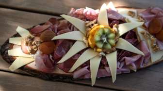 Ein kunstvoll angerichtetes Holzbrett mit verschiedenen Wurstsorten und Käse, serviert auf einem Holztisch