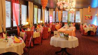 Festlich dekorierter Gastraum mit runden Tischen, bunter Tischdeko und Kronleuchtern