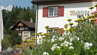Traditionelles Berggasthaus mit rotem Fensterladen und blühenden Blumen im Vordergrund