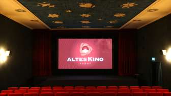 Kinosaal des Alten Kino Vaduz mit roten Kinosesseln, einer Bühne mit rotem Vorhang und einer blauen Decke mit goldenen Sternenmotiven.
