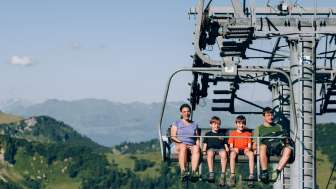 Eine Familie fährt mit der Sesselbahn Sareis über eine grüne Berglandschaft